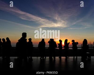 Silhouette d'un groupe de personnes ayant un repos pendant un congrès avec le coucher du soleil dans le contexte plusieurs d'entre eux de prendre des photos avec un téléphone cellulaire Banque D'Images