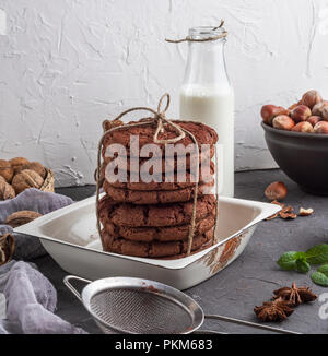 Pile de cookies aux pépites de chocolat dans un bol de fer blanc, derrière une bouteille de lait Banque D'Images