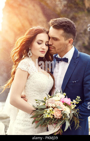 Couple hugging au coucher du soleil, les amoureux couple coucher du soleil. Cérémonie de mariage en plein air. Belle mariée et le marié avec bouquet de fleurs. Mariage blanc Banque D'Images