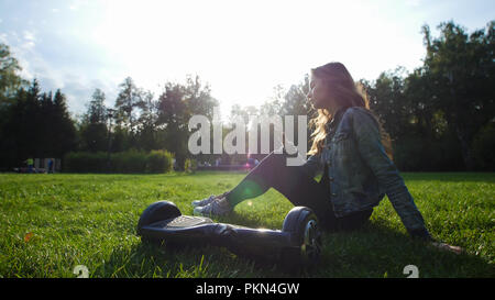 Jeune fille assise sur l'herbe, de tenir le téléphone dans ses mains. Le gyroscope est à côté de ses pieds. Banque D'Images