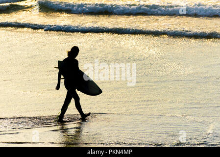 Surf Cornwall. La silhouette d'un surfer carrying his surfboard et marcher dans la mer à la plage de Fistral Newquay en Cornouailles. Banque D'Images