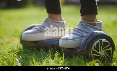 Les jambes des femmes dans sneakers sur un gyro dans le parc au milieu de l'herbe Banque D'Images