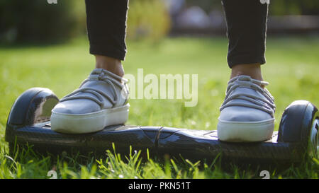 Fille dans sneakers sur un gyroscope au milieu de l'herbe dans le parc. dans le cadre des jambes Banque D'Images