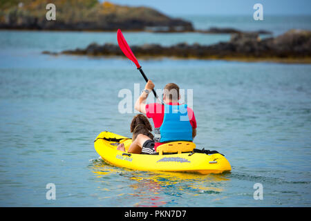 Vue arrière de l'homme en gilet de sauvetage, en vacances, assis avec un chien en kayak jaune, au bord de la mer, pagayant en mer. Vacances d'été au Royaume-Uni. Banque D'Images