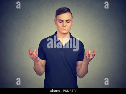 Jeune homme concentré se tenant la main dans la méditation en gardant les yeux fermés sur fond gris Banque D'Images