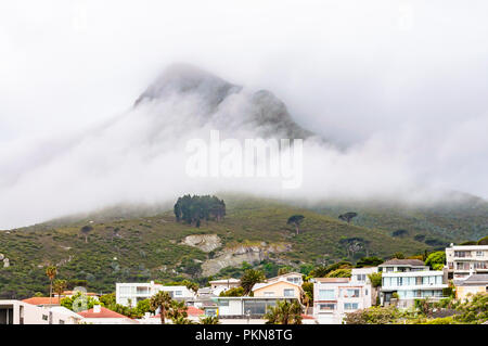 Les nuages et la montagne de la table couverte de brouillard derrière les maisons à Camps Bay, Afrique du Sud Banque D'Images