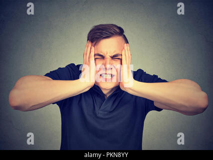 Jeune homme souffrant de douleur et le stress et réduit la tête avec les mains sur fond gris Banque D'Images