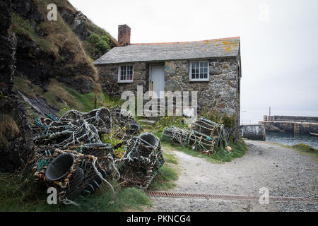 Une construction en pierre, petite maison de pêcheur de homards et les casiers à l'extérieur, sur le pittoresque port de Mullion Cove à Cornwall, uK. Banque D'Images