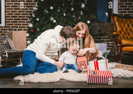 Célébration de la famille soirée de Noël. Famille trois peuples caucasiens assis sous conifère arbre de Noël sur marbre de tapis de laine. Tenir un enfant Banque D'Images