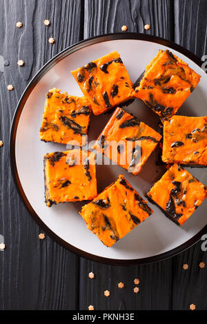 Fromage à la crème dessert Halloween Brownies composé d'un moelleux au chocolat noir garni d'une couche de cheesecake orange gros plan sur une assiette. Haut vertical Banque D'Images