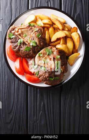 Ossobuco jarret avec une garniture de tranches de pommes de terre frites et les tomates sur une assiette sur la table. Haut Vertical Vue de dessus Banque D'Images