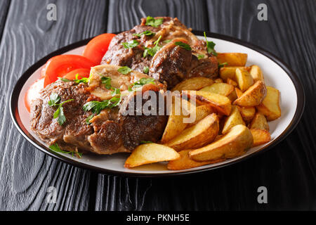 Pavé de boeuf Ossobuco avec pommes de terre rissolées et tomates fraîches libre sur une plaque sur une table horizontale. Banque D'Images