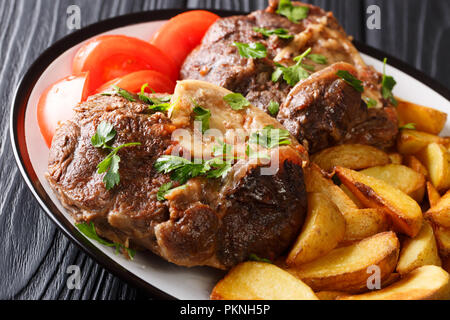 Délicieux steak poêlé servi Ossobuco tranches de pommes de terre et tomates fraîches close-up sur une plaque sur la table horizontale. Banque D'Images