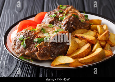 Repas copieux : veau rôti servi Ossobuco tranches de pommes de terre et tomates fraîches close-up sur une plaque sur la table horizontale. Banque D'Images