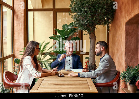 Déjeuner d'affaires. Trois personnes dans le restaurant sitting at table buvant un café chaud discuter projet joyeux. Concept de travail d'équipe Banque D'Images