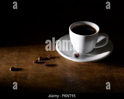 Le café dans une tasse à café avec des haricots sur la table en bois. Banque D'Images
