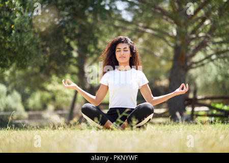 Jeune femme arabe faisant du yoga dans la nature. Le port de l'Afrique du Nord vêtements sport lotus faisant figure de parc urbain. Banque D'Images