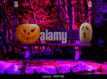 Deux citrouilles Halloween effrayant gravés sur un banc de parc dans un paysage de forêt spooky Banque D'Images