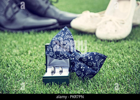 Les anneaux de mariage, noeud papillon et des femmes et des chaussures d'hommes sur l'herbe verte. Symbole de l'amour. Blue photo filtre. Banque D'Images