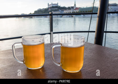 Pichets de bière placée sur une table de bois sur fond de Danube et le château de Bratislava, Slovaquie Banque D'Images