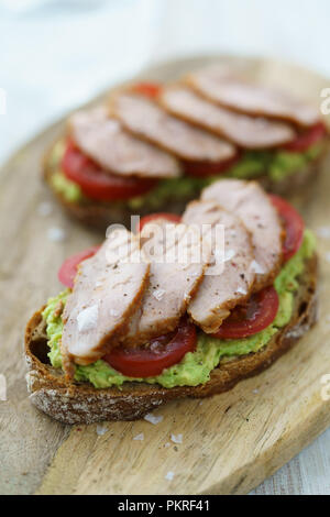 Filet mignon de porc sandwich avec la purée d'avocat, tomates et sel Maldon. Servi sur une planche à découper en bois, haute résolution. Banque D'Images