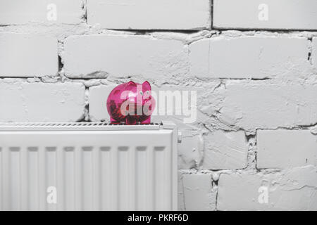 Coûts de chauffage - tirelire sur le radiateur à l'avant du mur en brique blanche Banque D'Images