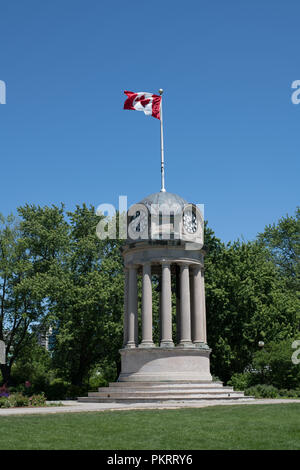 Brandir le drapeau canadien sur le dessus d'une horloge et clocher dans un parc avec des arbres en arrière-plan Banque D'Images