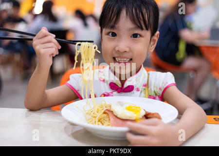 Chinois asiatique little girl eating noodles with chopsticks in restaurant Banque D'Images