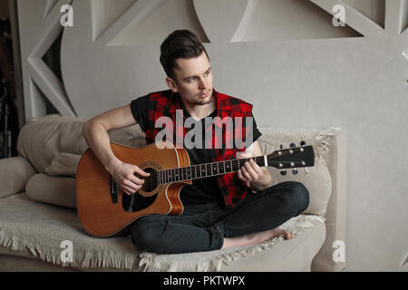 Beau jeune homme assis sur un canapé et jouer de la guitare Banque D'Images