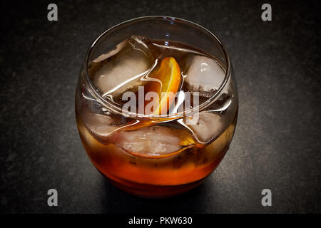 Un cas isolé de verre clair, orange / brown boisson alcoolisée avec de la glace et les tranches d'orange sur un fond noir Banque D'Images