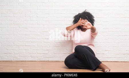 Young african american woman assis sur le plancher à la maison couvrant les yeux avec les mains et faire cesser de geste avec l'expression triste et la peur. Un embarras Banque D'Images