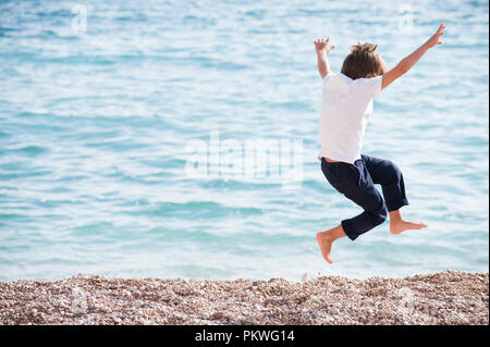 Petit garçon sain et actif en chemise blanche et le pantalon de sauter sur mer à l'automne Banque D'Images