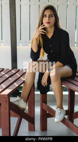 Jeune fille à l'appareil photo alors qu'il était assis sur une table en bois dans un balcon. Banque D'Images