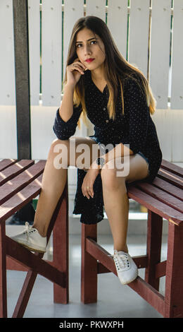 Jeune fille à l'appareil photo alors qu'il était assis sur une table en bois dans un balcon. Banque D'Images