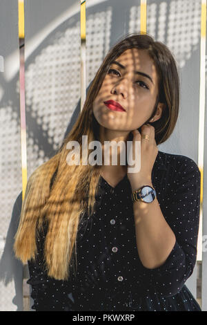 Jeune femme regardant la caméra avec l'ombre de fenêtre sur mur. Banque D'Images