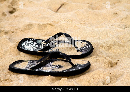 Designer noir tongs dans sand at beach Banque D'Images