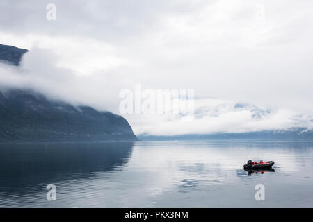 Petit bateau sur un lac calme brumeux avec des montagnes en arrière-plan Banque D'Images