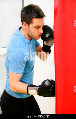 Male boxer de la formation est l'entraînement avec sac de boxe au gymnase club. Portrait d'une jeune athlète beau homme sports boxe gants rouge dans la pratique Banque D'Images