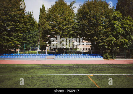 Stand bleu large ligne sièges tourné en parc avec terrain de sport vert Banque D'Images