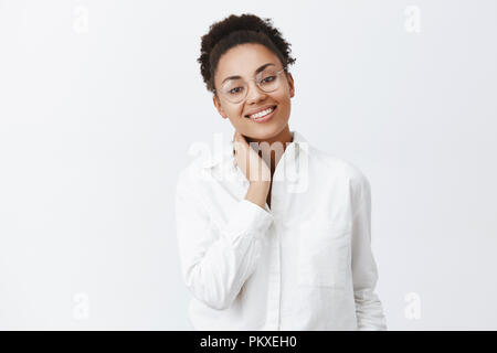 Assez mignon copine revenir à la maison après le travail, voir ami faire le dîner, se sentir joyeux. Femme douce africains-américains dans les verres et de collaborateur shirt, touchant le cou et regarder l'appareil photo Banque D'Images