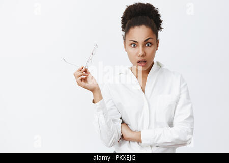 Soeur, ce qui est arrivé. Surpris et étonné de la peau sombre amie en chemise blanche, prendre des verres de surprise et de choc, à l'écoute des histoires étonnantes sur fond gris Banque D'Images