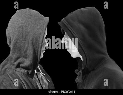 Deux adolescents en difficulté avec capuche noir debout en face de l'autre en profil isolé sur fond noir. Image en noir et blanc. Banque D'Images