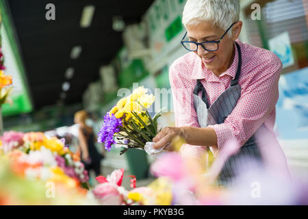 Charrming femme senior sales fleurs sur le marché local Banque D'Images