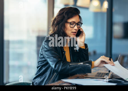 Asian Business Woman talking on cell phone tout en travaillant au bureau. La lecture de certains documents cadres féminins et talking on mobile phone. Banque D'Images