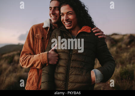Heureux l'homme et la femme debout sur une montagne à l'écart et souriant. Couple chaud à porter debout sur la montagne et profiter de la vue. Banque D'Images