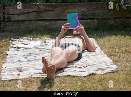 Jeune homme couché de soleil sur tapis jardin lire un livre scolaire le soleil d'été, UK Banque D'Images