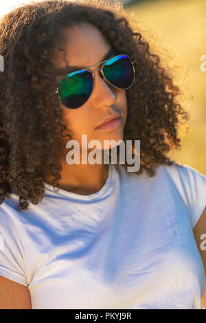 Belle course mixte African American female adolescent fille jeune femme portant des lunettes de soleil aviateur bleu réfléchissant à au coucher et au lever du soleil Banque D'Images