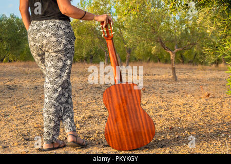 Jeune femme debout avec une guitare classique espagnole ou dans une campagne andalouse d'oliviers au coucher du soleil. Banque D'Images