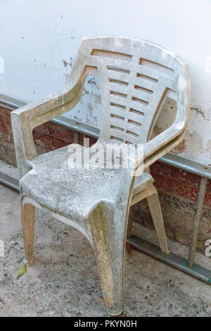 Une vue en gros plan de deux très vieilles chaises en plastique blanc contre le côté d'une échelle en métal et mur blanc Banque D'Images