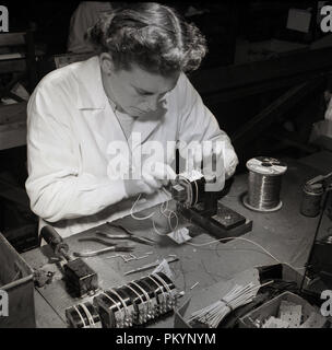 Années 1950, photo historique montrant une femme portant un manteau blanc et assis à un établi de décisions par main, composants pour Bush Radio, un des leaders de l'électronique grand public de la société de cette époque. Banque D'Images